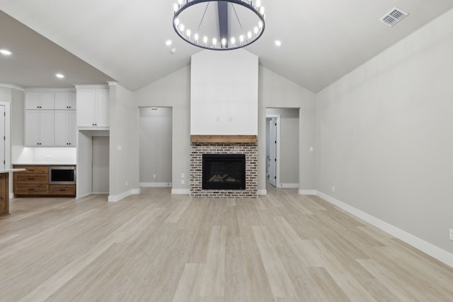 unfurnished living room featuring light hardwood / wood-style floors, lofted ceiling, a fireplace, and an inviting chandelier