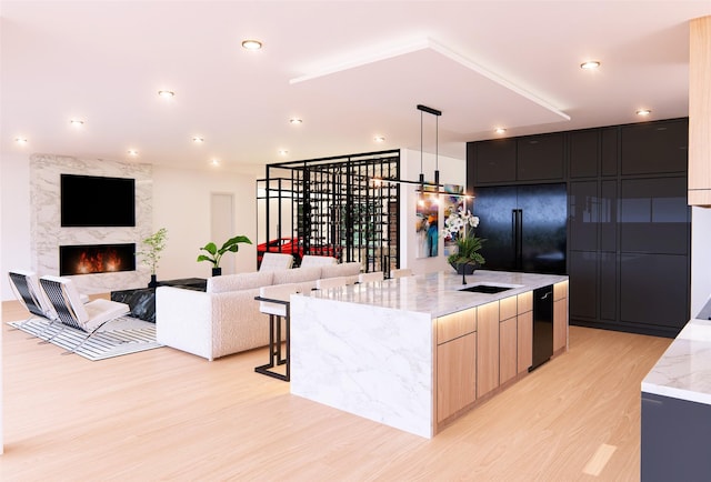 kitchen featuring a kitchen island with sink, black fridge, light wood-type flooring, light brown cabinetry, and light stone counters