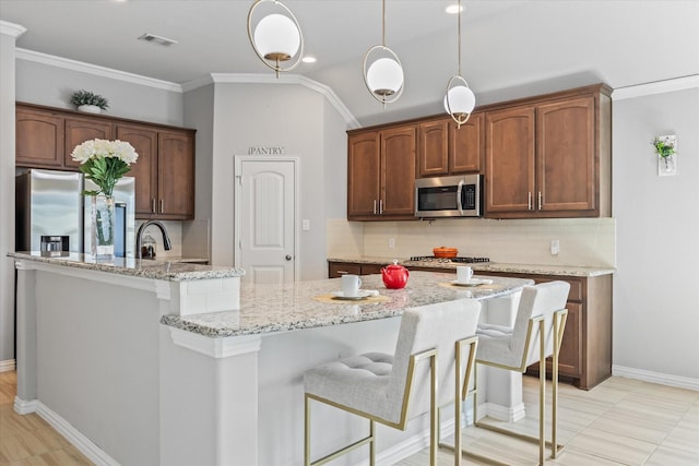 kitchen featuring an island with sink, backsplash, ornamental molding, stainless steel appliances, and light stone countertops