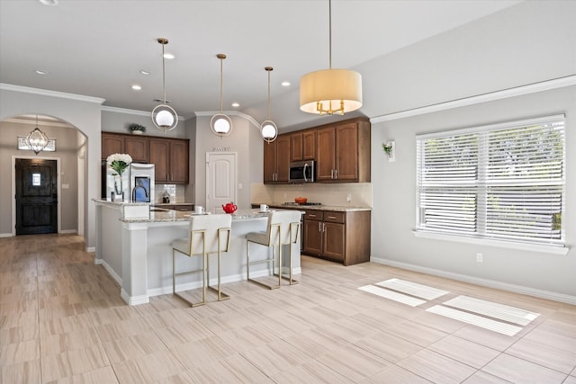 kitchen with sink, light stone counters, decorative light fixtures, a center island with sink, and backsplash