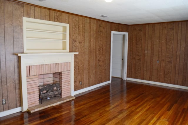 unfurnished living room featuring a fireplace, crown molding, wooden walls, and dark hardwood / wood-style floors