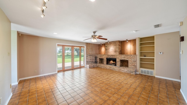 unfurnished living room featuring built in shelves, ceiling fan, tile patterned flooring, and a brick fireplace