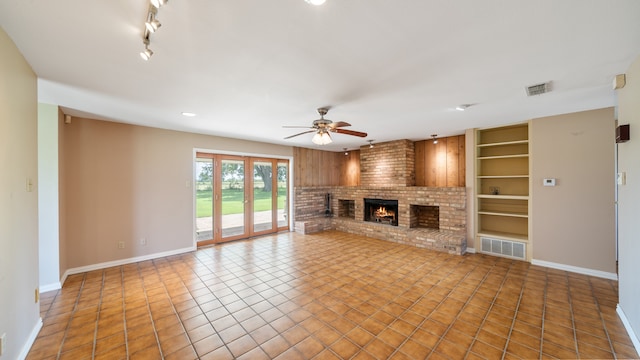 unfurnished living room with a brick fireplace, ceiling fan, tile floors, rail lighting, and built in shelves