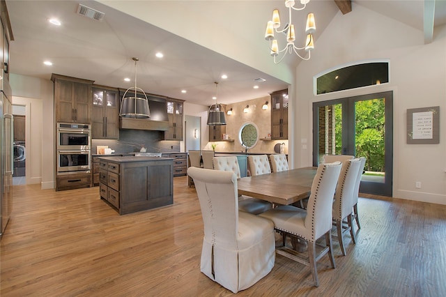 dining space with lofted ceiling with beams, washer / dryer, light wood-type flooring, and an inviting chandelier