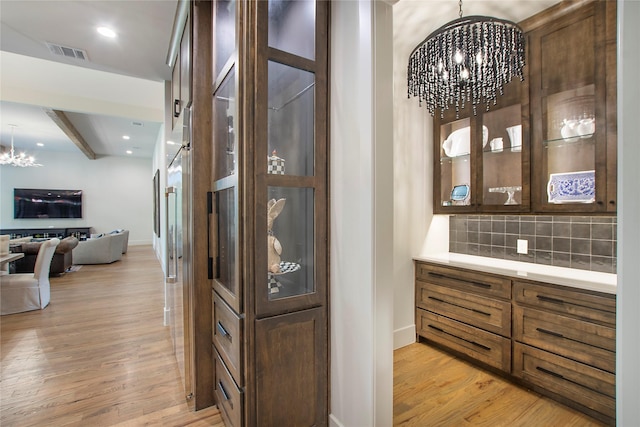 bar with a notable chandelier, decorative backsplash, light wood-type flooring, and hanging light fixtures