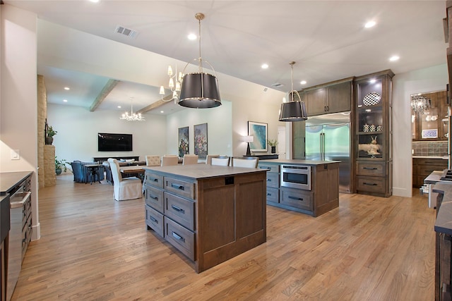 kitchen with pendant lighting, dark brown cabinetry, built in appliances, and a center island