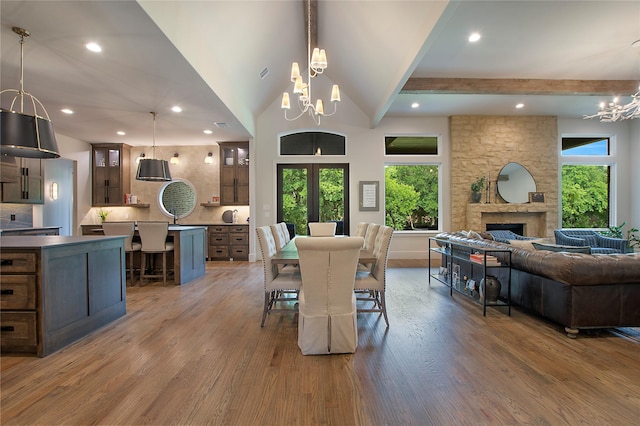 dining space featuring wood-type flooring, a stone fireplace, a wealth of natural light, and a notable chandelier