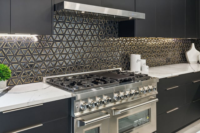 kitchen featuring decorative backsplash, light stone counters, range with two ovens, and range hood