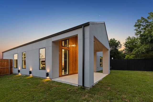 back house at dusk with a patio area and a yard