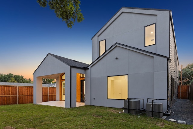 back house at dusk with a lawn, central AC unit, and a patio