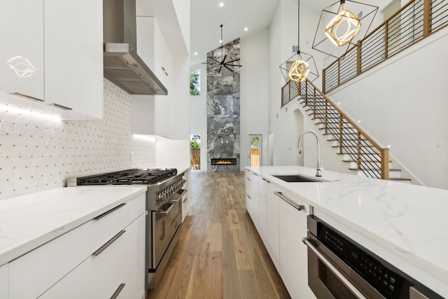 kitchen with white cabinets, appliances with stainless steel finishes, wall chimney exhaust hood, hanging light fixtures, and a chandelier