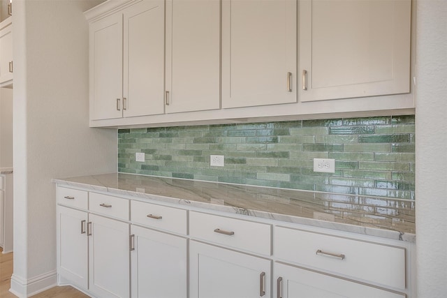 kitchen with white cabinetry, light stone counters, and backsplash