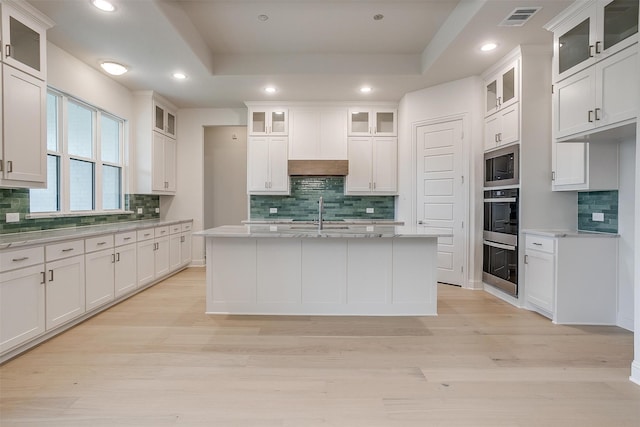 kitchen with white cabinetry, light hardwood / wood-style floors, a center island with sink, and tasteful backsplash