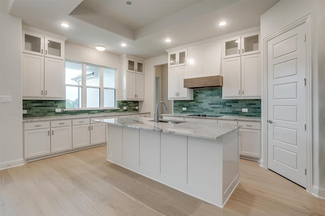 kitchen with a center island with sink, decorative backsplash, sink, light stone countertops, and white cabinetry