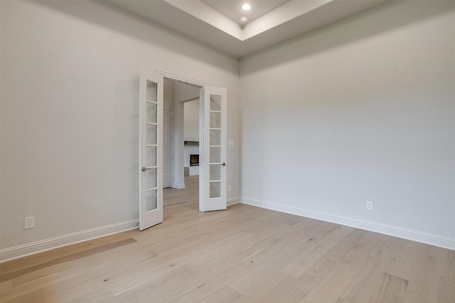 spare room featuring french doors, light wood-type flooring, and a raised ceiling