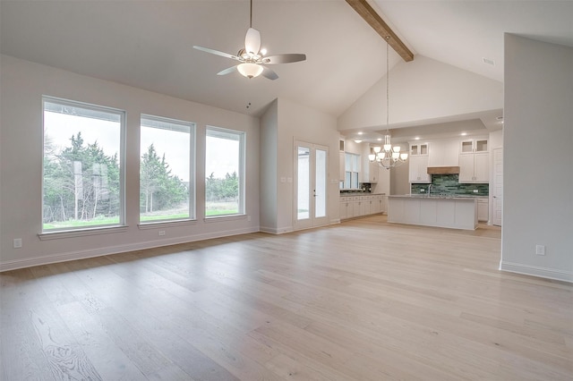 unfurnished living room with ceiling fan with notable chandelier, a wealth of natural light, light hardwood / wood-style floors, and beam ceiling