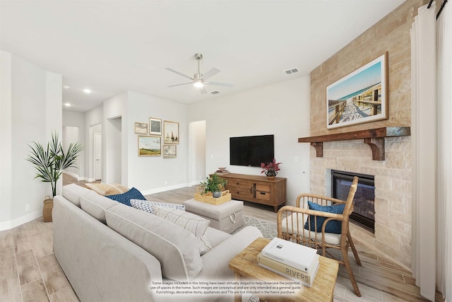 living room featuring a stone fireplace, light wood-type flooring, and ceiling fan