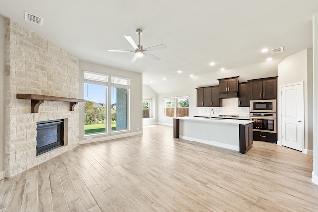 kitchen featuring a stone fireplace, stainless steel appliances, sink, light wood-type flooring, and ceiling fan