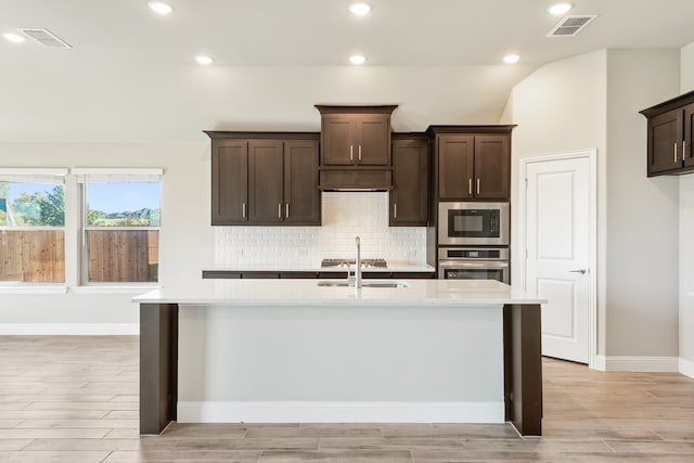 kitchen featuring light hardwood / wood-style floors, stainless steel appliances, dark brown cabinets, and a kitchen island with sink