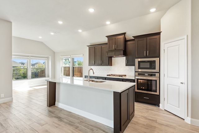 kitchen with sink, a kitchen island with sink, stainless steel appliances, and vaulted ceiling