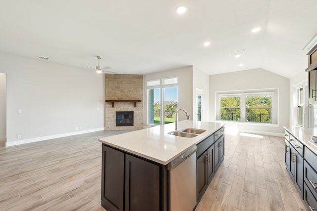 kitchen featuring an island with sink, light hardwood / wood-style flooring, sink, stainless steel dishwasher, and a fireplace