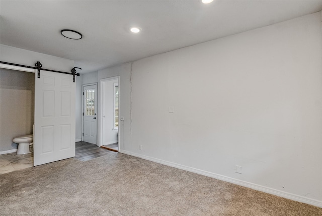 unfurnished bedroom with ensuite bathroom, a barn door, and carpet