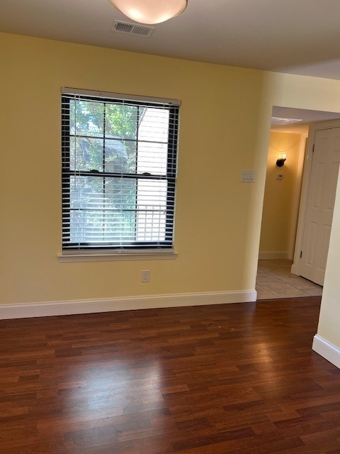 spare room with wood finished floors, visible vents, and baseboards