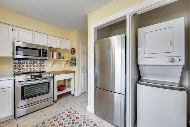 kitchen with white cabinetry, backsplash, stacked washer / drying machine, light tile patterned flooring, and appliances with stainless steel finishes