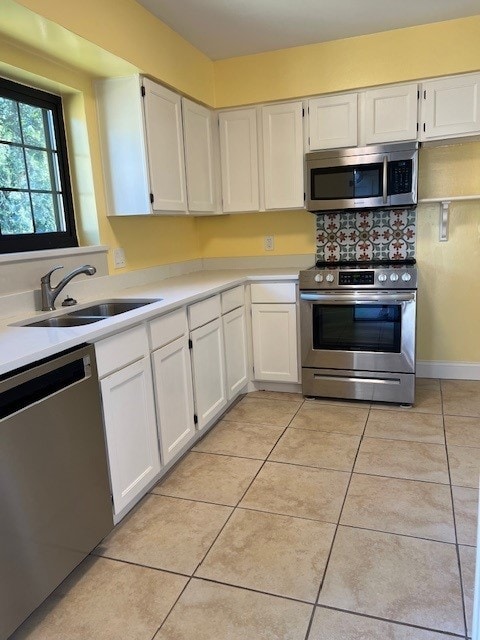 kitchen with light tile patterned floors, a sink, light countertops, white cabinets, and appliances with stainless steel finishes