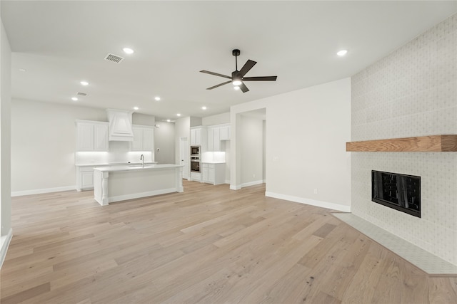 unfurnished living room with a tiled fireplace, sink, light wood-type flooring, and ceiling fan