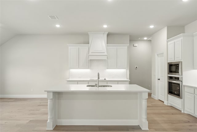 kitchen featuring oven, an island with sink, black microwave, sink, and light wood-type flooring