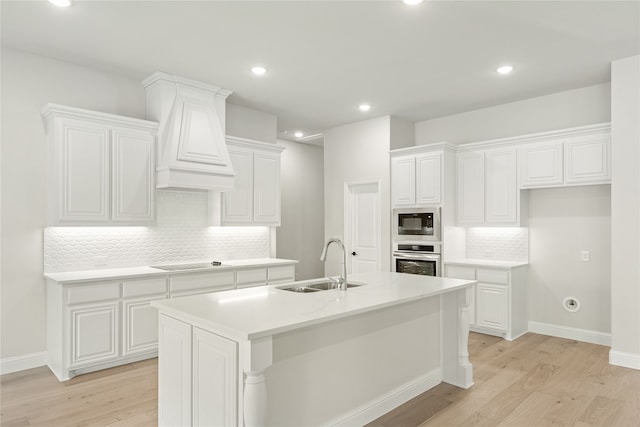 kitchen with stainless steel oven, a center island with sink, sink, built in microwave, and light hardwood / wood-style floors