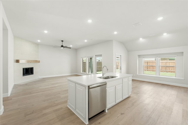 kitchen featuring an island with sink, light wood-type flooring, stainless steel dishwasher, white cabinetry, and a fireplace