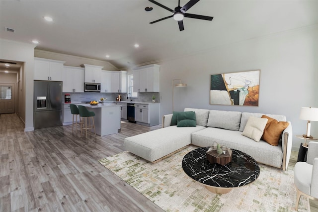 living room featuring lofted ceiling, sink, crown molding, ceiling fan, and light wood-type flooring