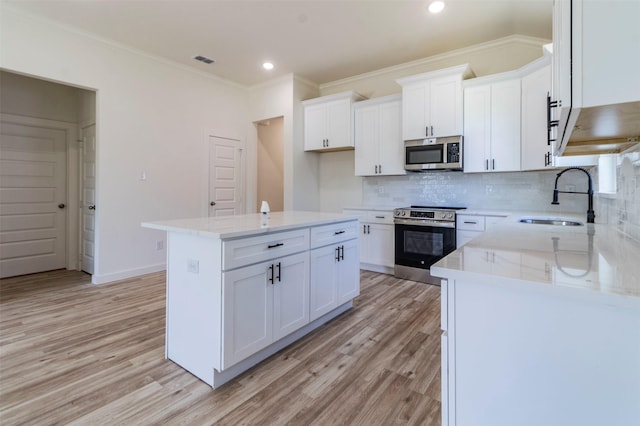 kitchen with an island with sink, appliances with stainless steel finishes, sink, and white cabinets