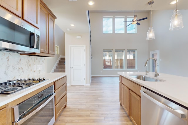 kitchen featuring decorative backsplash, hanging light fixtures, light hardwood / wood-style flooring, sink, and stainless steel appliances