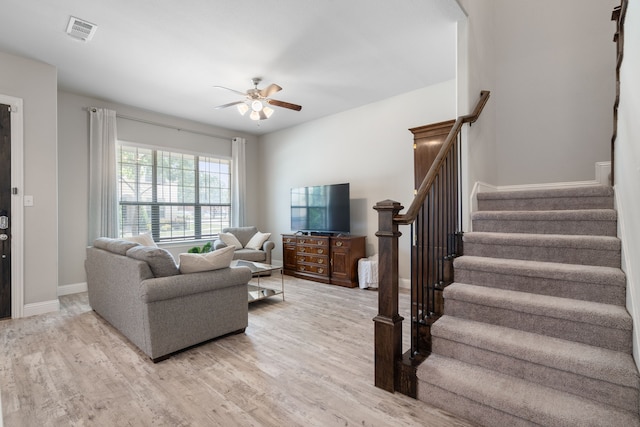 living room featuring ceiling fan, stairway, visible vents, and light wood-style floors