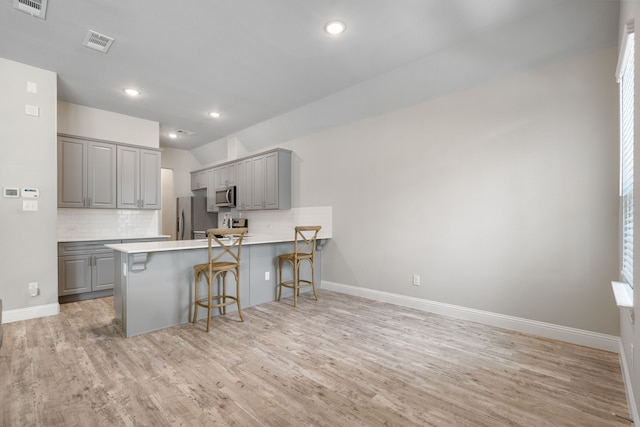 kitchen featuring gray cabinetry, a breakfast bar, tasteful backsplash, kitchen peninsula, and stainless steel appliances