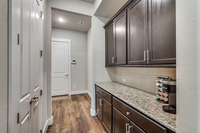 bar featuring light stone counters, dark brown cabinetry, dark hardwood / wood-style flooring, and decorative backsplash