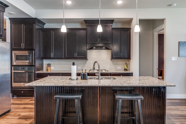 kitchen featuring stainless steel appliances, an island with sink, hanging light fixtures, and light hardwood / wood-style flooring