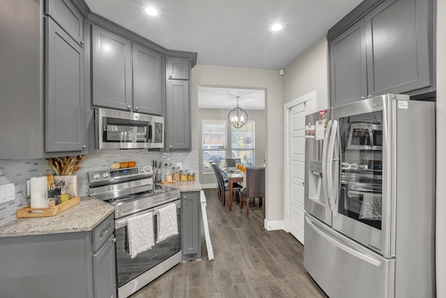 kitchen featuring light stone countertops, dark hardwood / wood-style floors, gray cabinets, decorative light fixtures, and stainless steel appliances