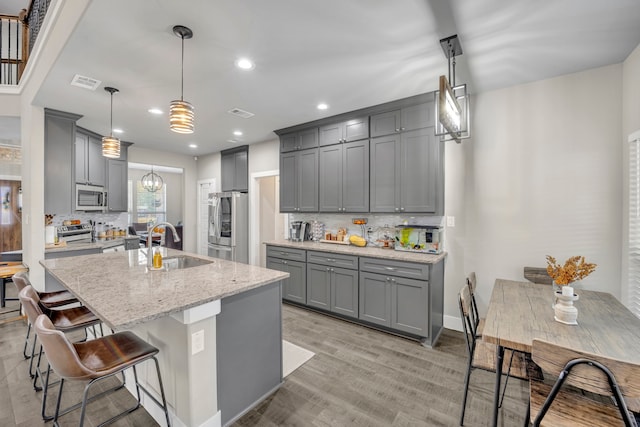 kitchen featuring gray cabinets, appliances with stainless steel finishes, decorative light fixtures, and tasteful backsplash