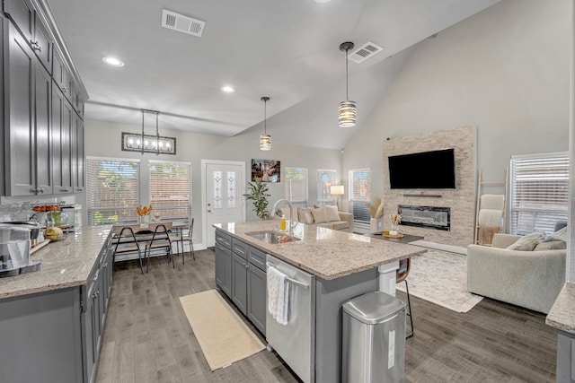 kitchen featuring gray cabinetry, an island with sink, a stone fireplace, dark hardwood / wood-style flooring, and pendant lighting