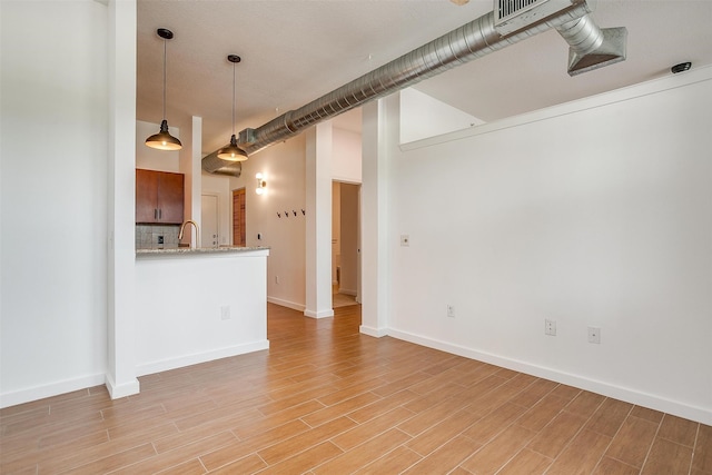 interior space with decorative backsplash, light hardwood / wood-style floors, kitchen peninsula, light stone countertops, and pendant lighting