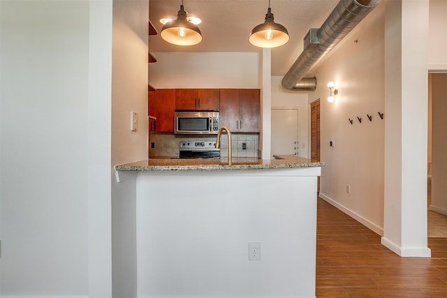 kitchen with a textured ceiling, kitchen peninsula, hanging light fixtures, stainless steel appliances, and hardwood / wood-style floors