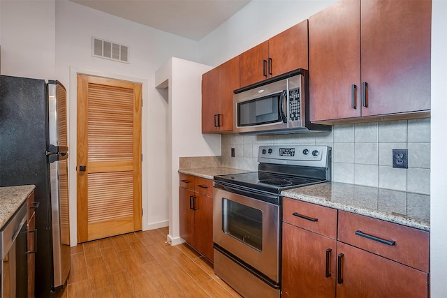 kitchen featuring light stone countertops, stainless steel appliances, light hardwood / wood-style floors, and decorative backsplash