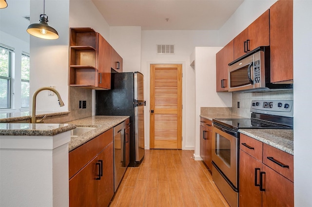 kitchen featuring sink, light stone counters, decorative light fixtures, appliances with stainless steel finishes, and light hardwood / wood-style floors