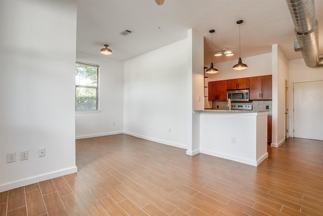 kitchen with hanging light fixtures, kitchen peninsula, backsplash, appliances with stainless steel finishes, and light hardwood / wood-style floors