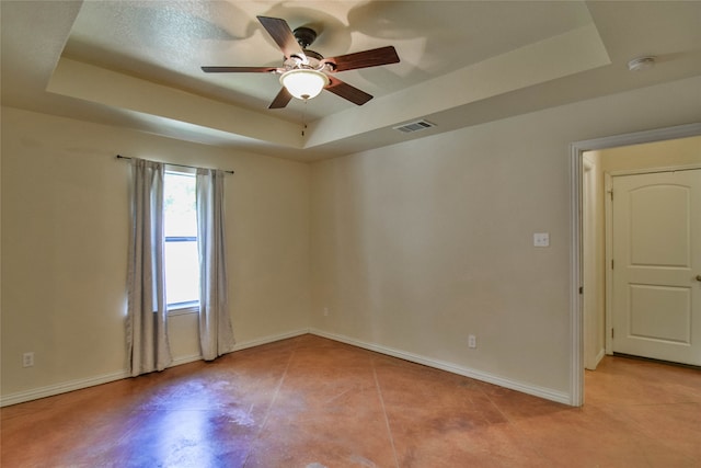 empty room with ceiling fan and a tray ceiling