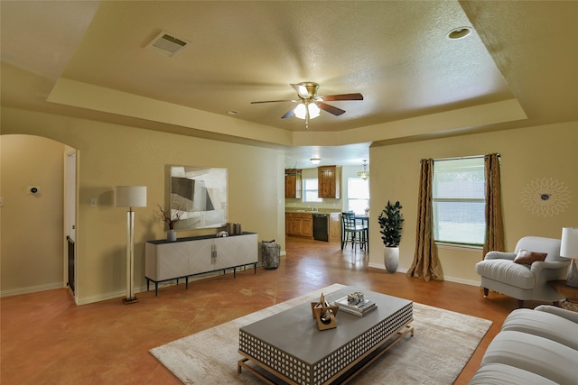 living room featuring a tray ceiling, ceiling fan, sink, and a textured ceiling